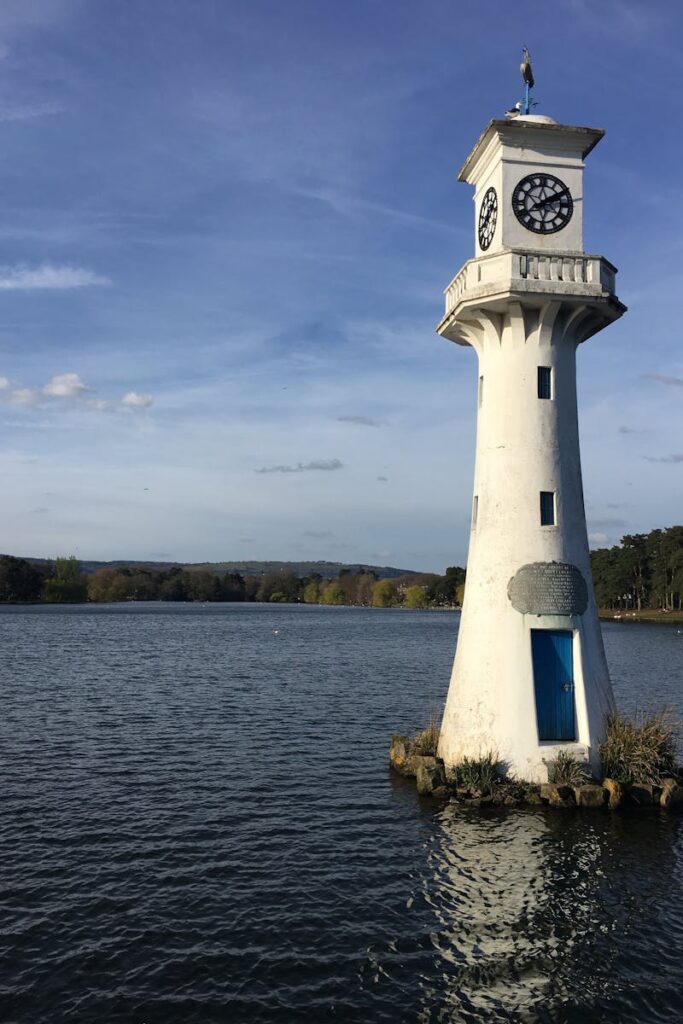 A tranquil scene of Scott Memorial Lighthouse at Roath Park Lake, Cardiff, under a clear sky.
