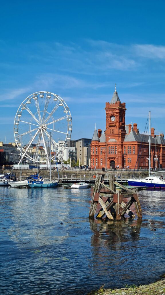 Explore the vibrant Cardiff Bay featuring a Ferris wheel, historic Pierhead Building, and tranquil reflections.