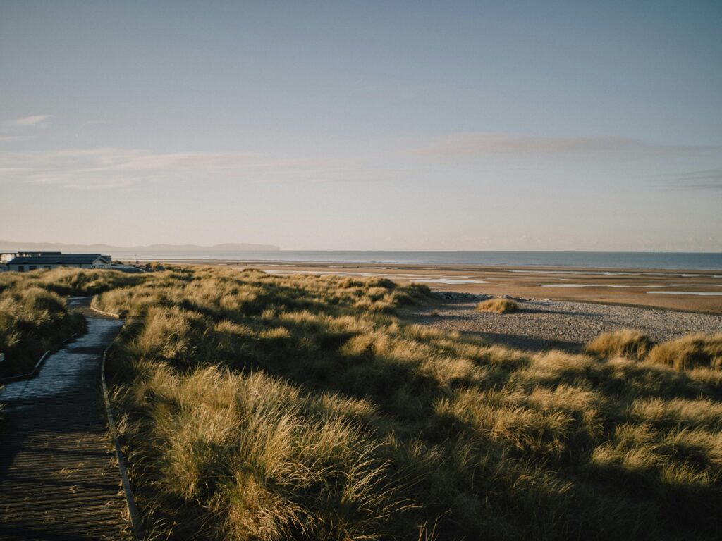Tranquil view of a wooden walkway and dunes at Rhyl beach, Wales, under clear skies.