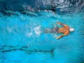 Top view of a swimmer wearing a cap, performing a front crawl stroke in a clear blue swimming pool. Swansea Swimming Pools
