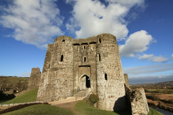 a castle with a walkway leading up to it. Kidwelly Castle